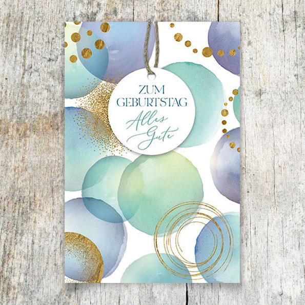 Vergrößerte Abbildung Geburtstagskarte mit zartem Aquarellmuster in Blautönen, goldener Folienprägung und rundem Anhänger an gold-brauner Kordel